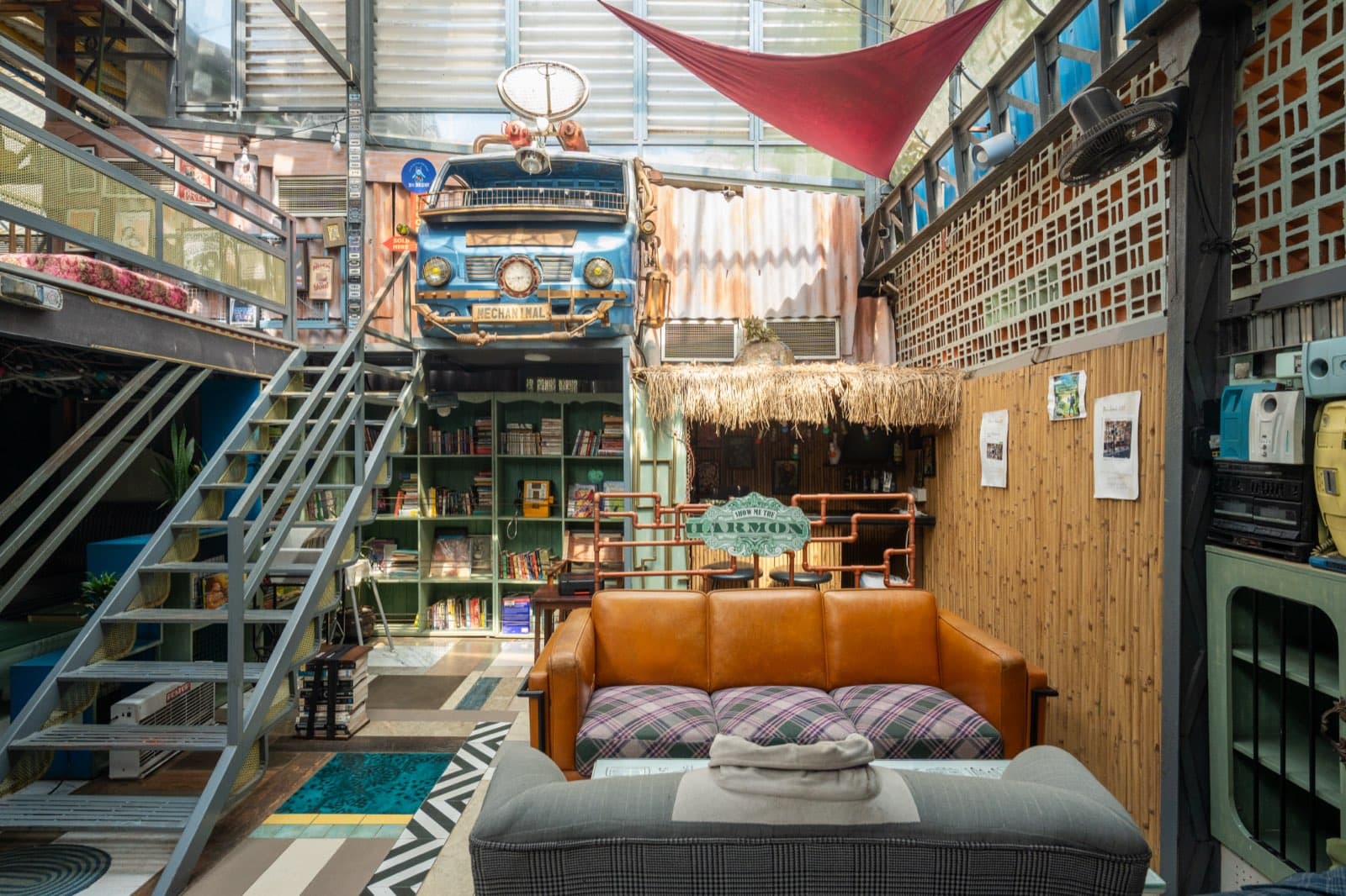A lounge beneath a mezzanine: a leather sofa, bookshelves, and the front of an old vehicle mounted on the wall above.