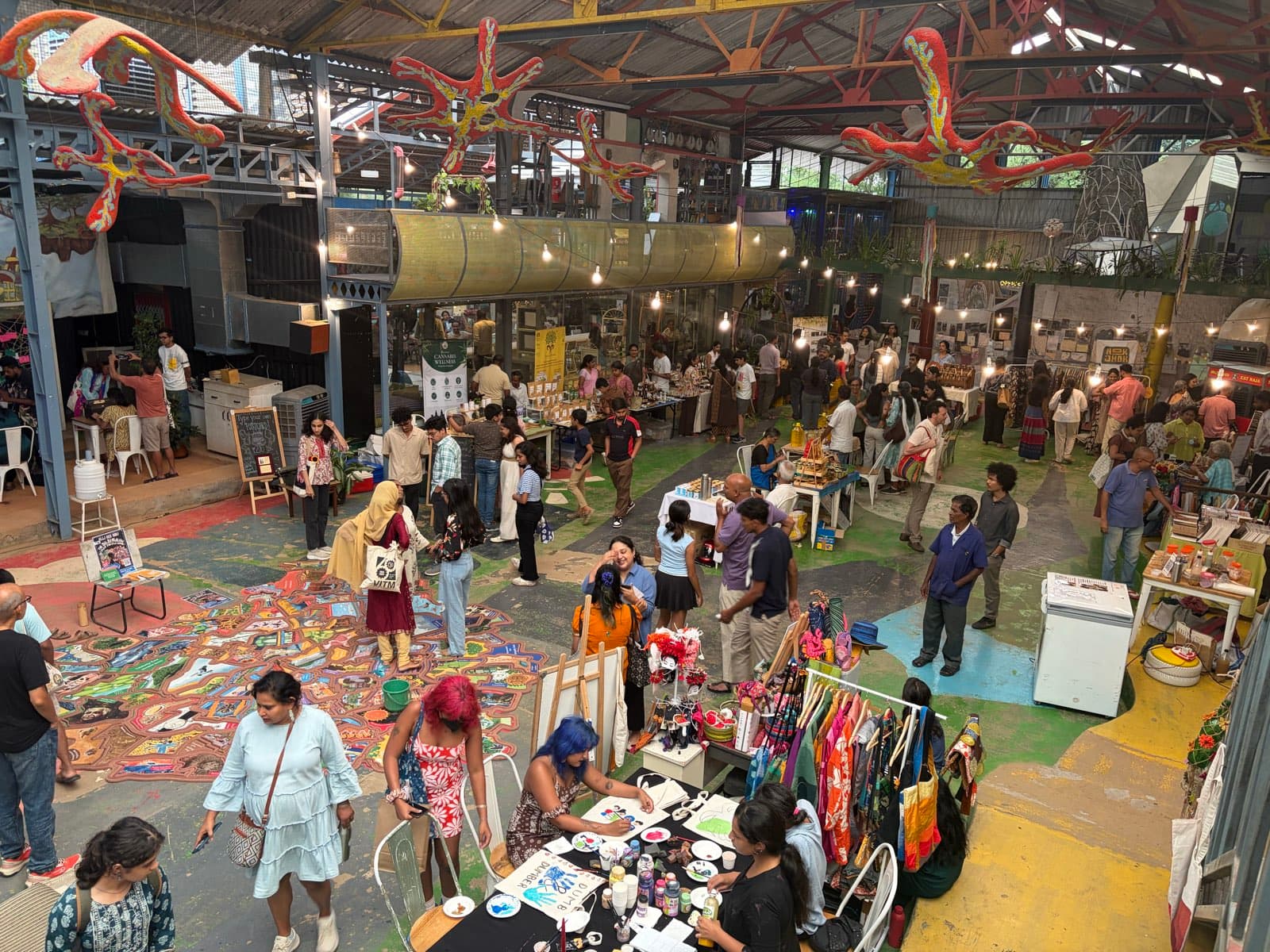 Seen from above, a busy market on the Bangalore Creative Circus's painted warehouse floor, with stalls and people moving between them.