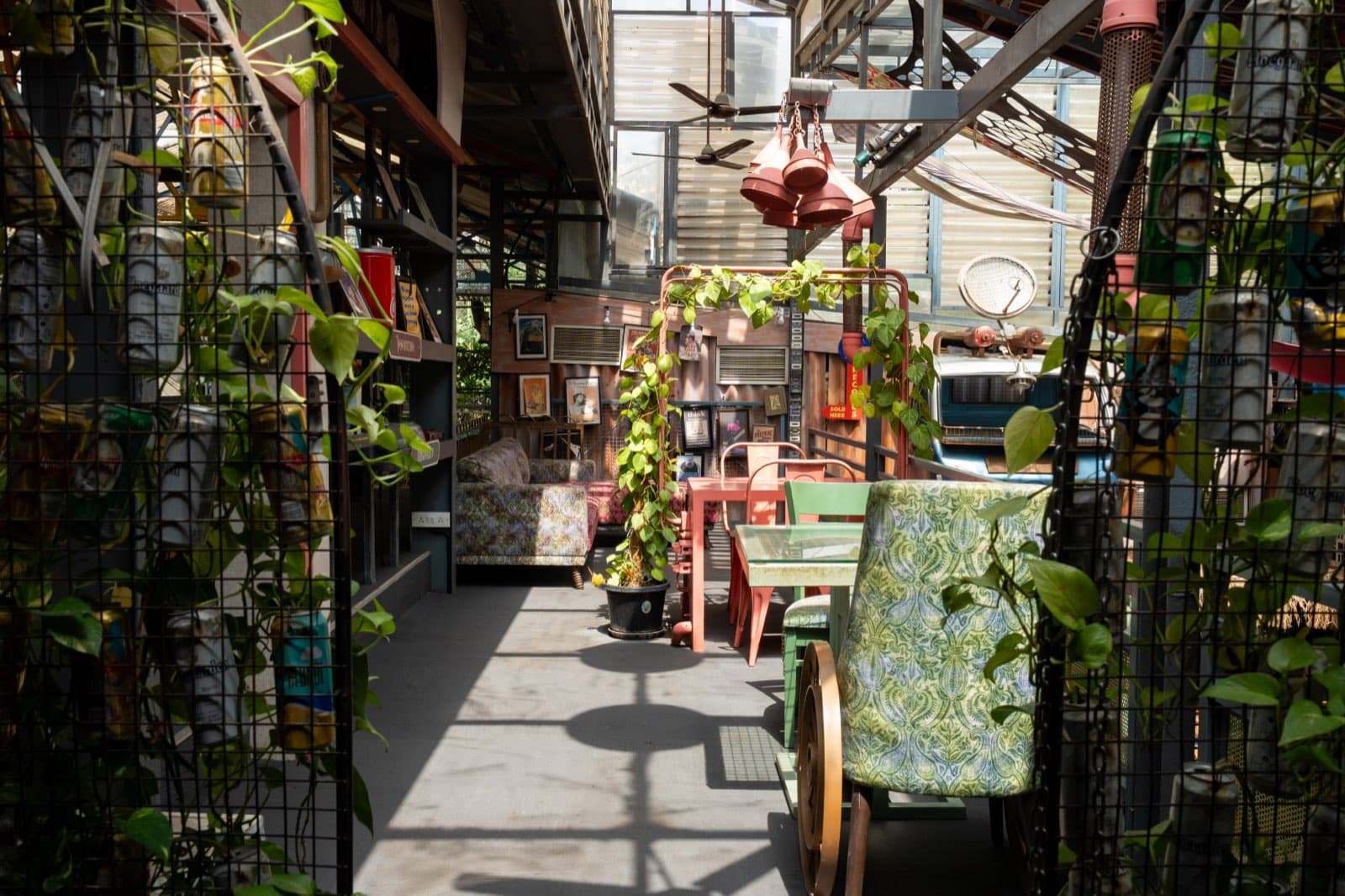 A plant-lined walkway through the warehouse, with repurposed furniture under a steel-and-mesh frame.